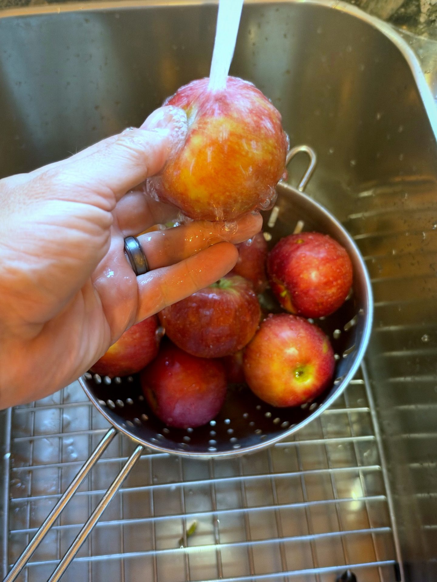 Washing a fresh red apple under the kitchen faucet