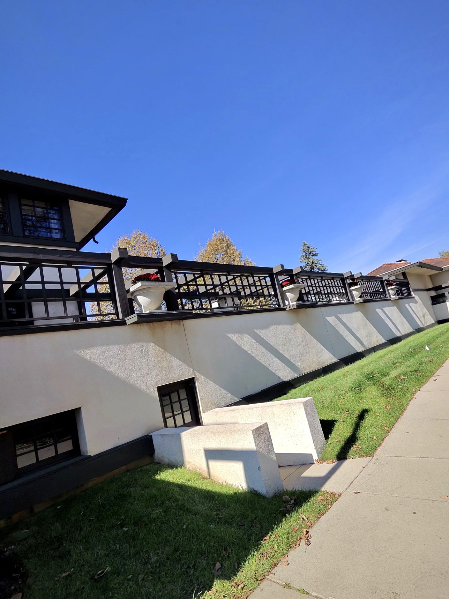 Side terrace of Westcott House with dark wood trellis, red flower urns, and cream stucco against blue sky