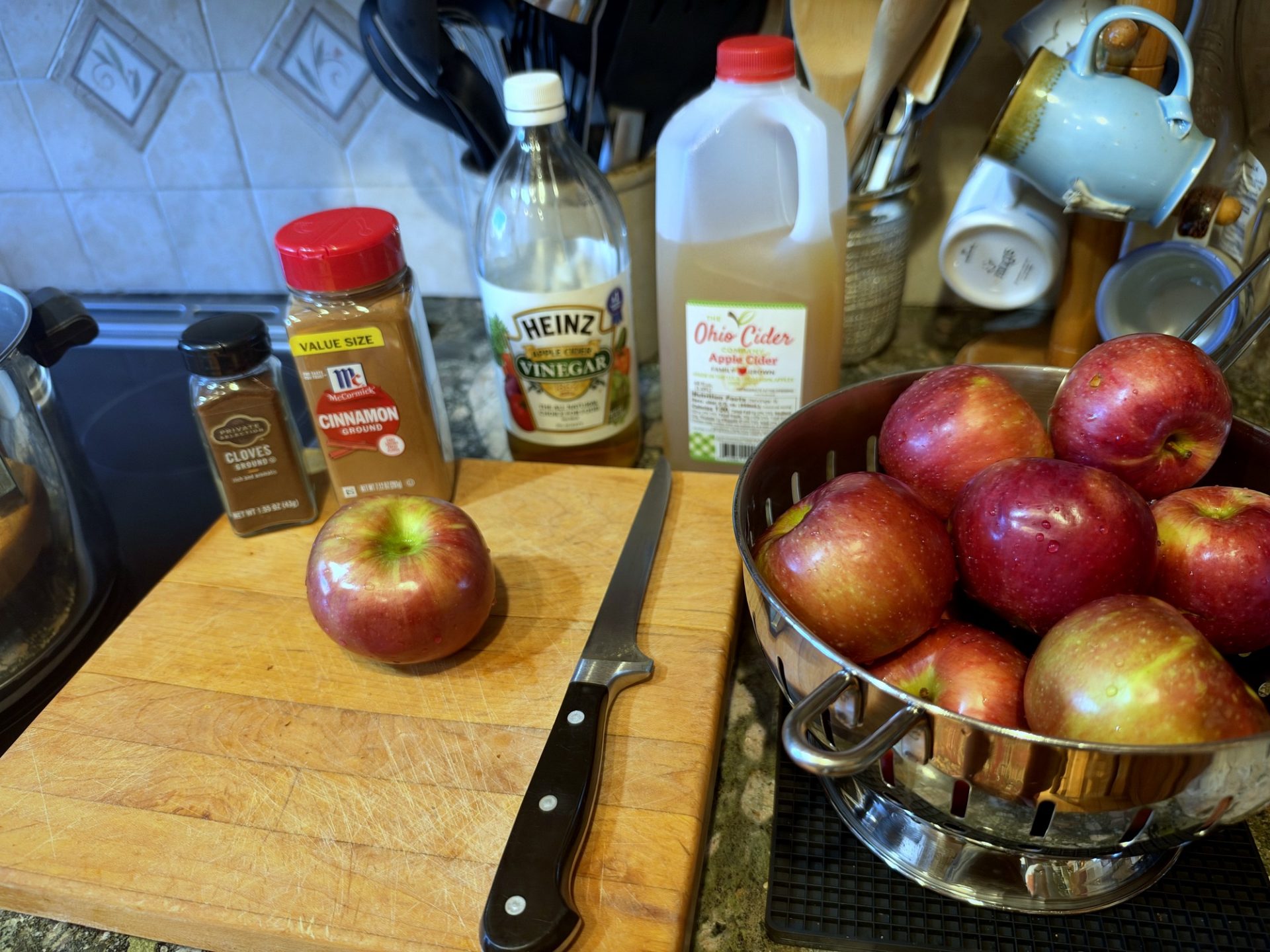 Apple butter ingredients: apples, cinnamon, cloves, vinegar, apple cider and a chef's knife on a cutting board