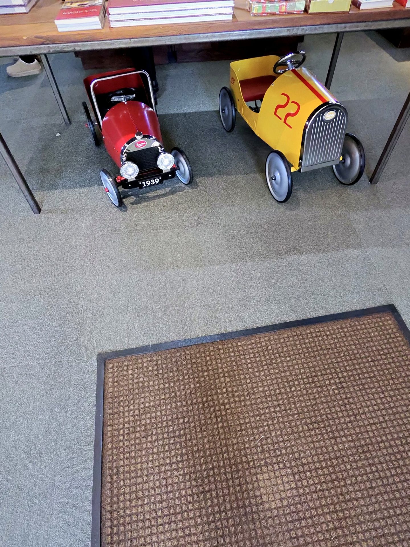 Red and yellow vintage-style pedal cars under the gift shop display table at Westcott House