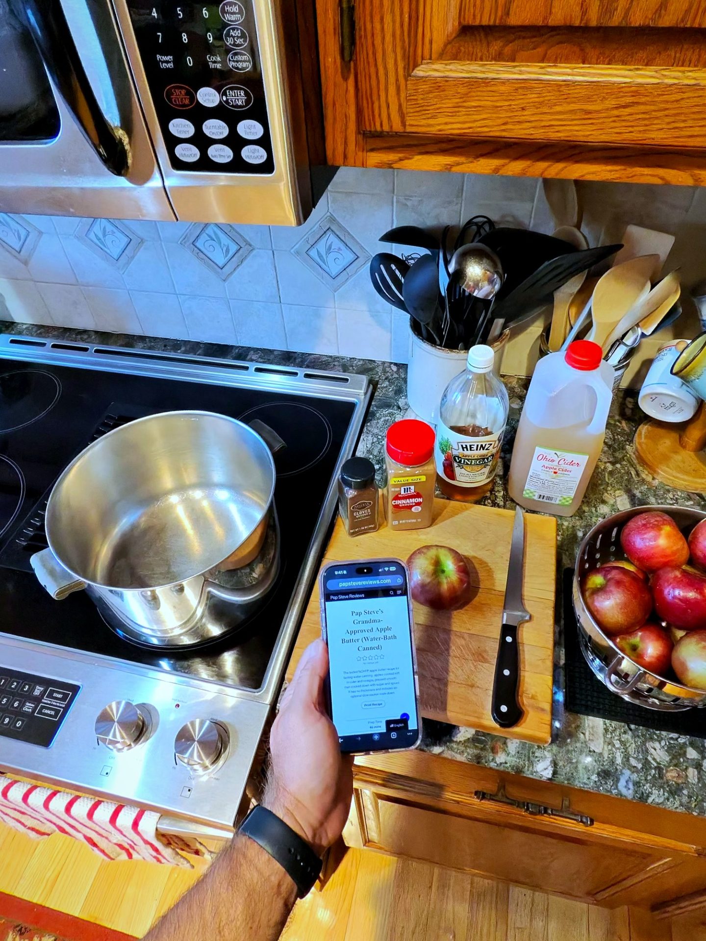 Stockpot heating on the stove with the apple butter recipe pulled up on a phone