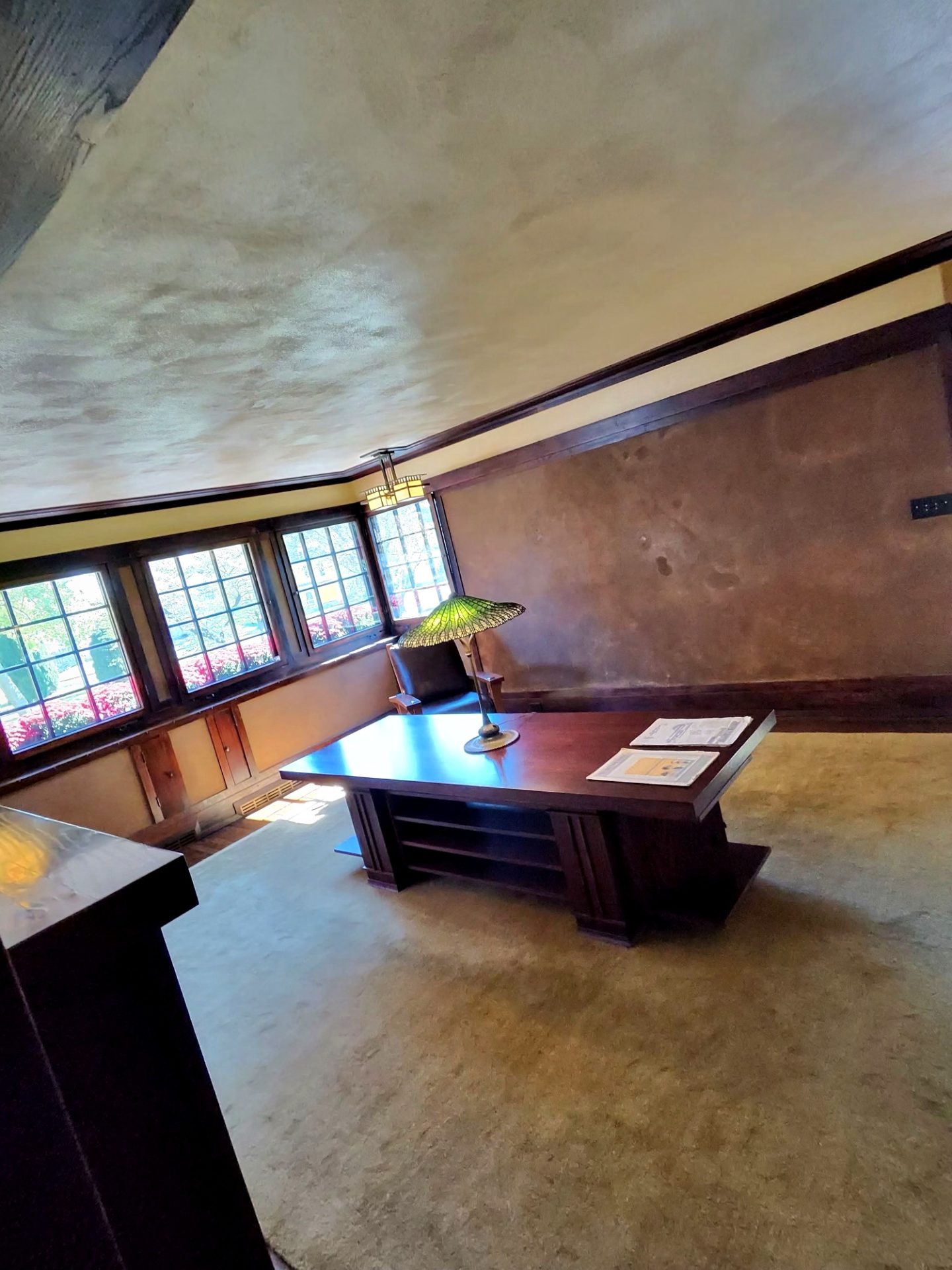 Study or library room with dark wood desk, green glass lamp, and casement windows at Westcott House
