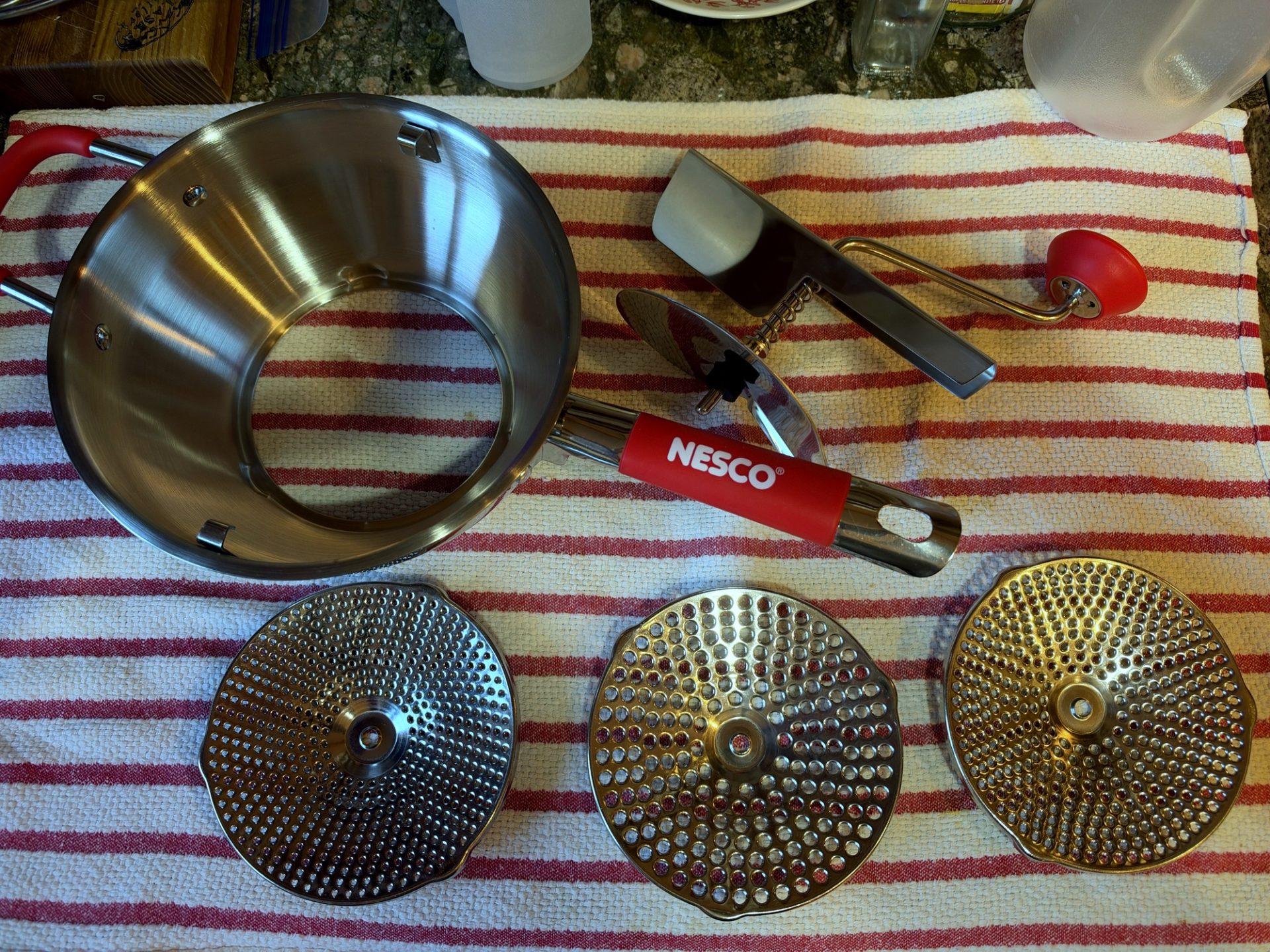 NESCO food mill parts and screens laid out on a striped towel