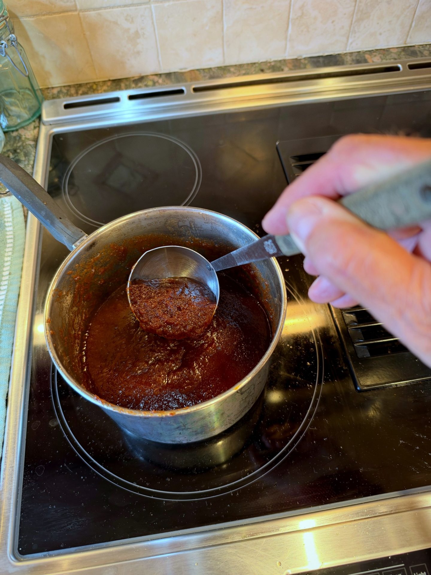 Ladling thick, dark apple butter from the pot