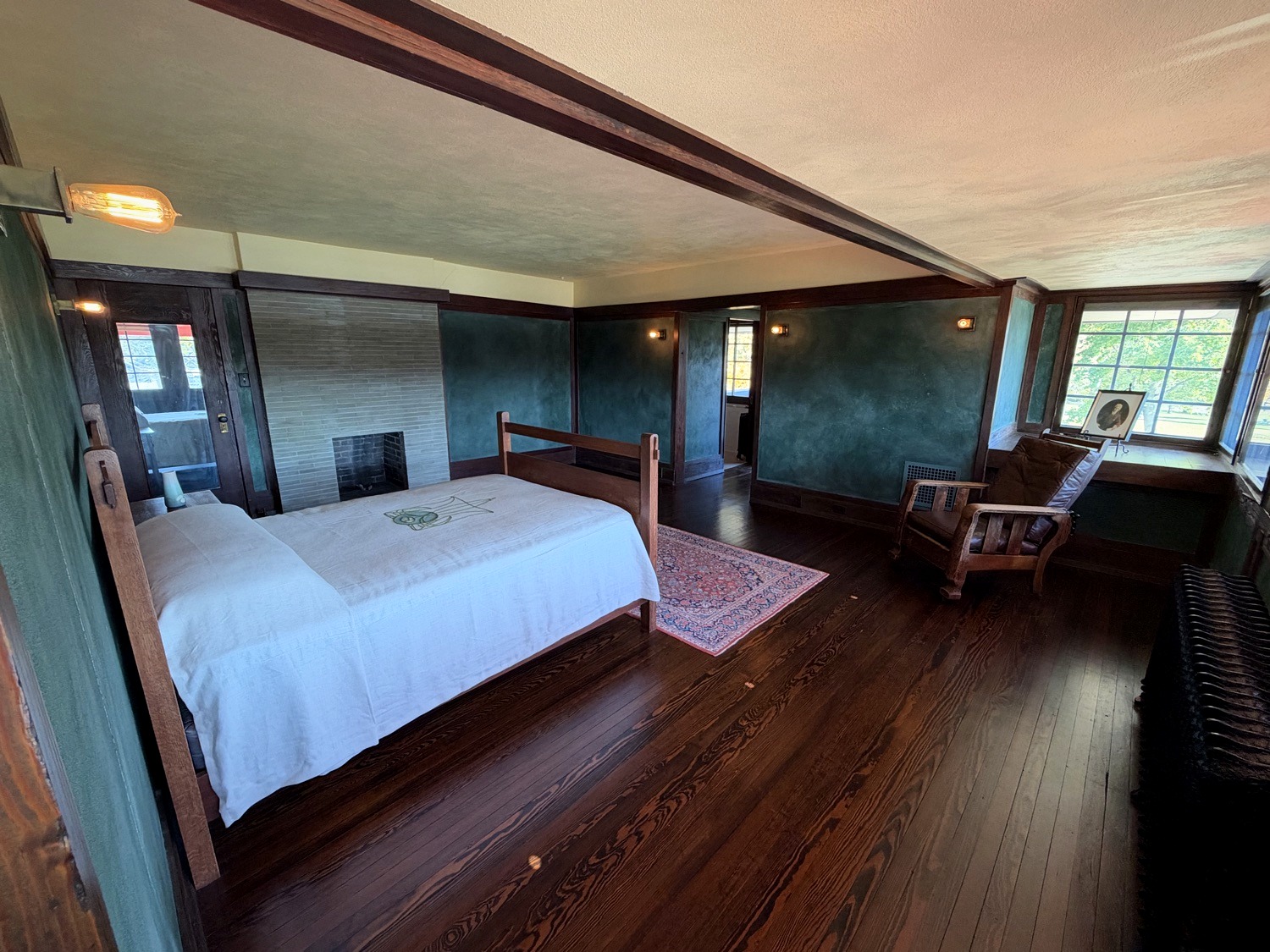 Master bedroom with green walls, dark wood trim, brick fireplace, and white bedspread at Westcott House