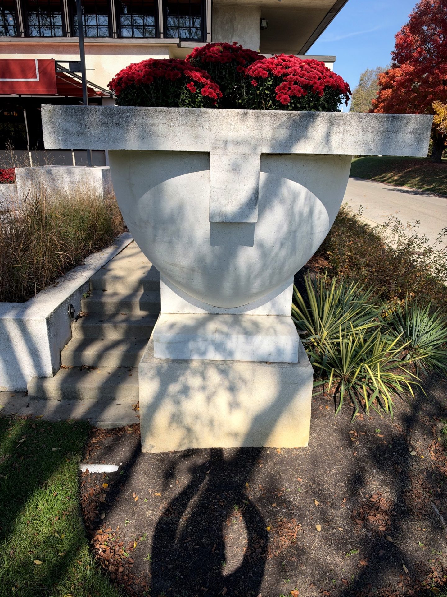Large white Prairie-style concrete planter filled with red chrysanthemums beside Westcott House