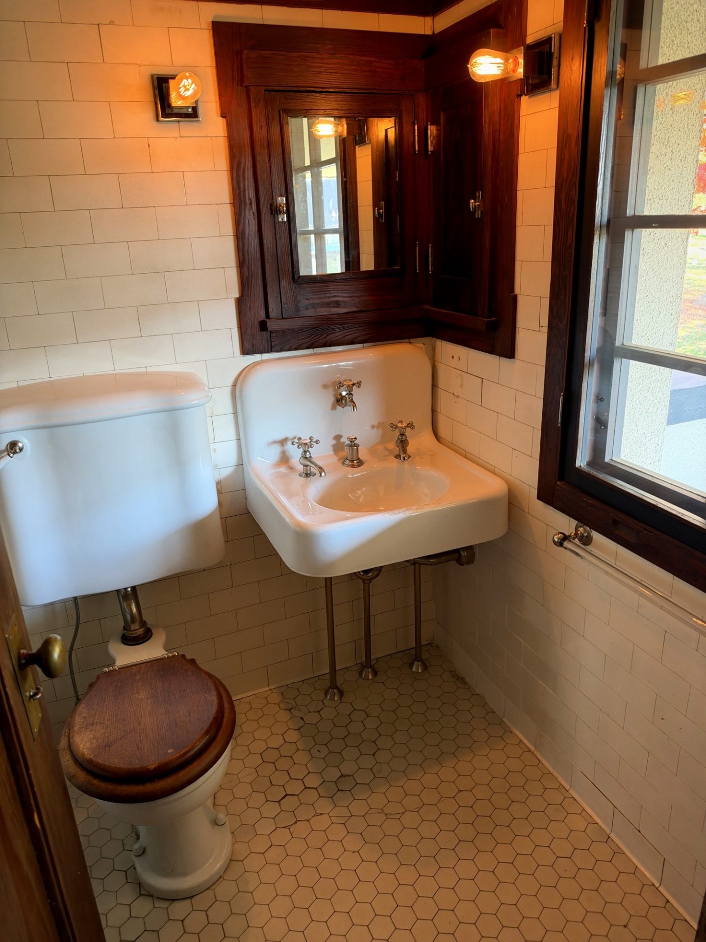 Historic Westcott House bathroom with pedestal sink showing three faucet handles, hexagonal floor tile, and wood-framed medicine cabinet