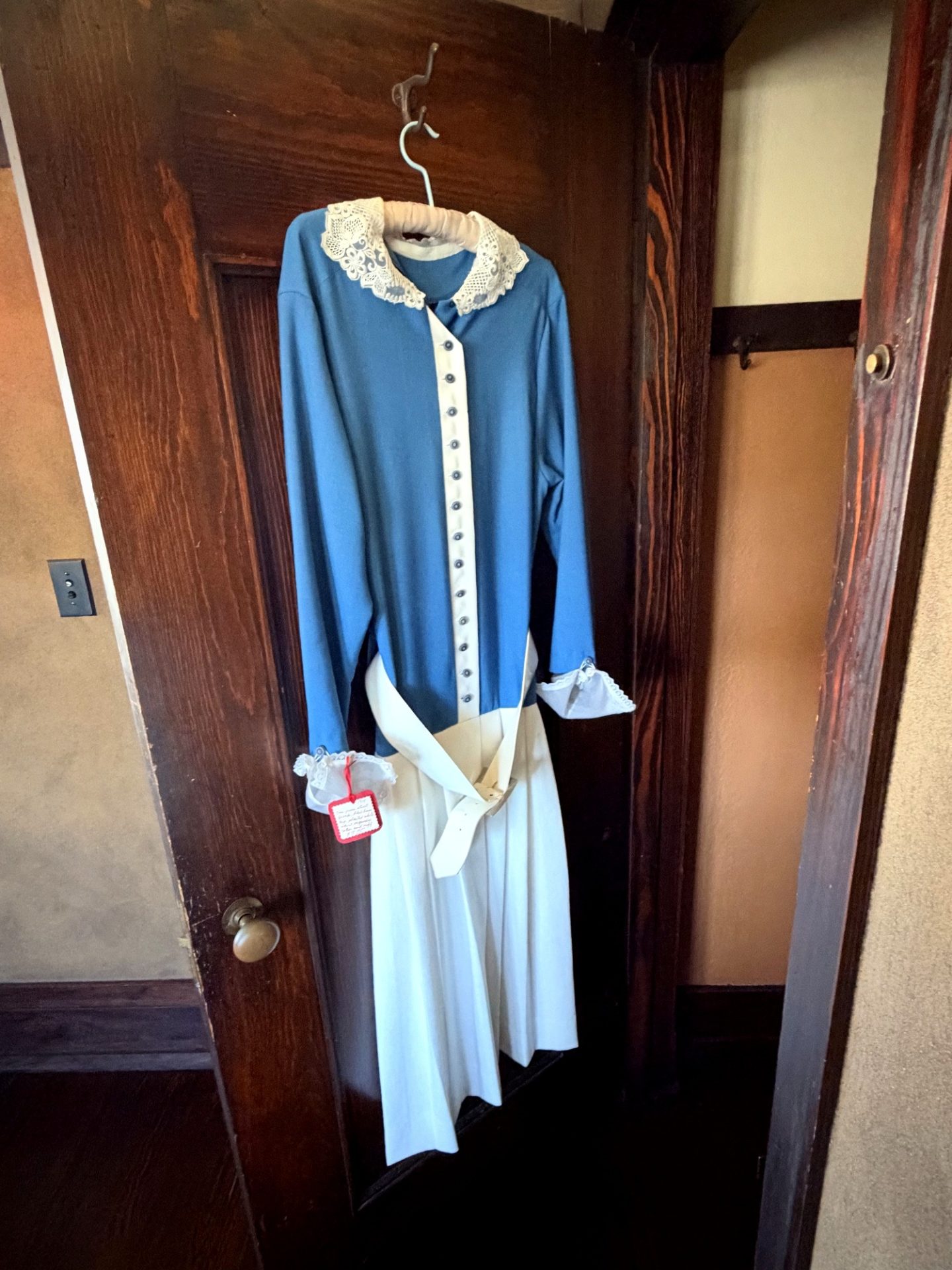 Blue and white period maid uniform hanging on a dark wood door at Westcott House