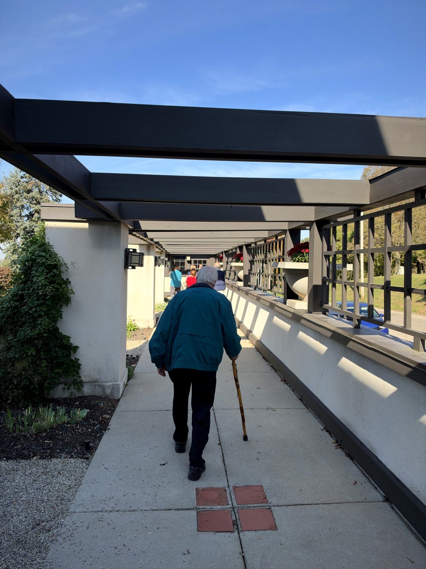 Man with white hair and cane walking down covered pergola walkway at Westcott House