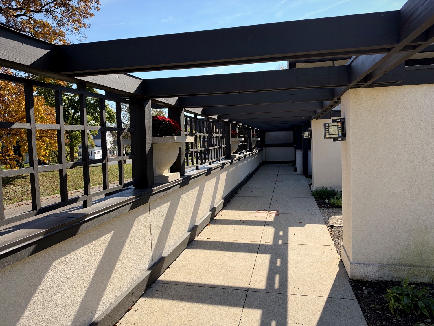 Long covered pergola walkway at Westcott House with mission lanterns and red mum urns