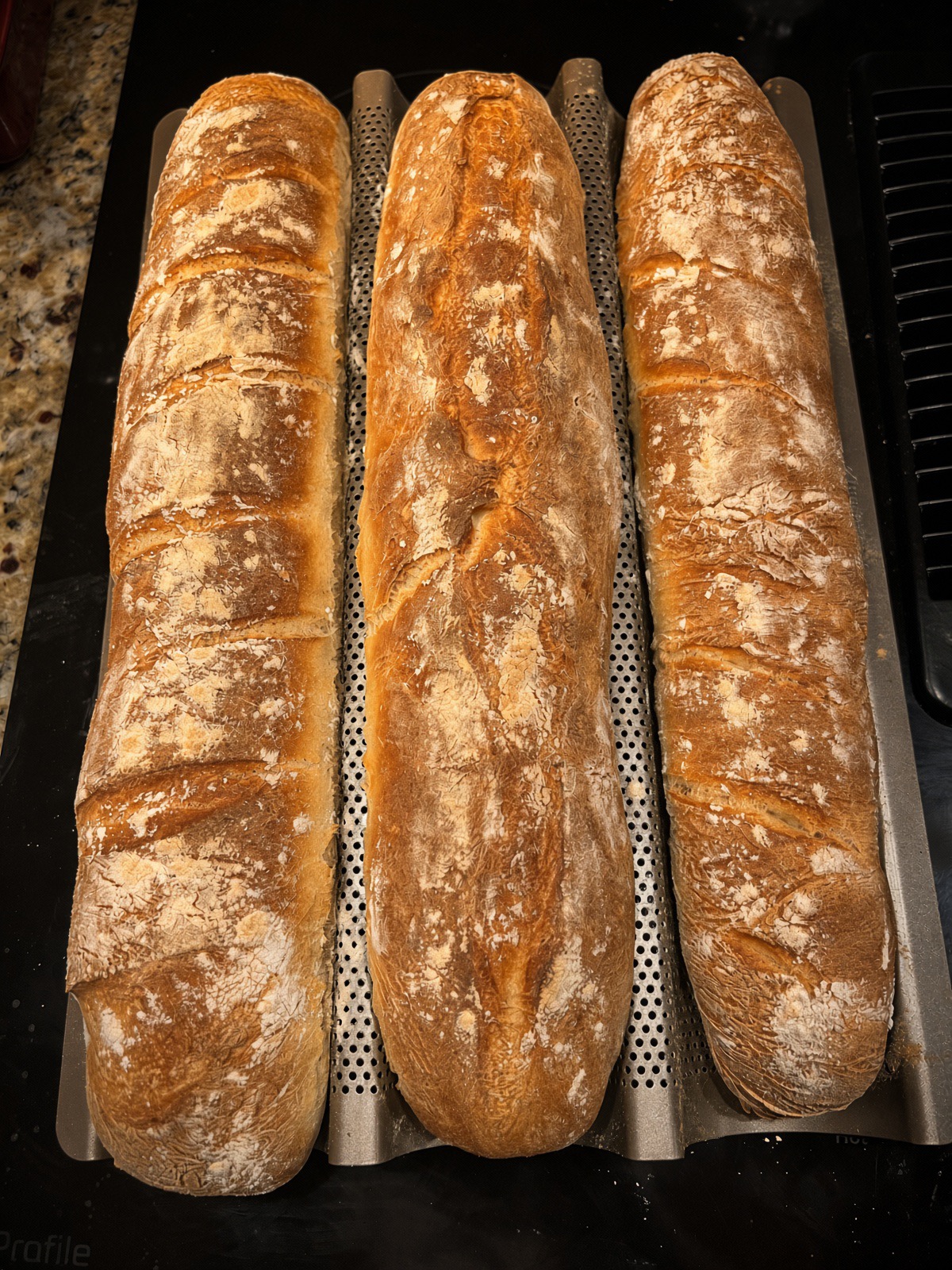 Three homemade baguettes fresh out of the oven on a perforated baguette pan