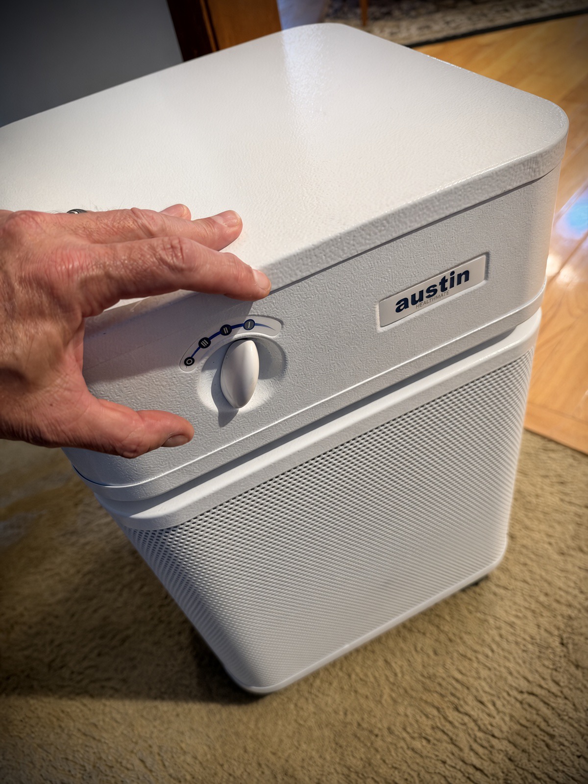 Hand reaching for the simple four-position control dial on top of a white Austin Air HealthMate air purifier