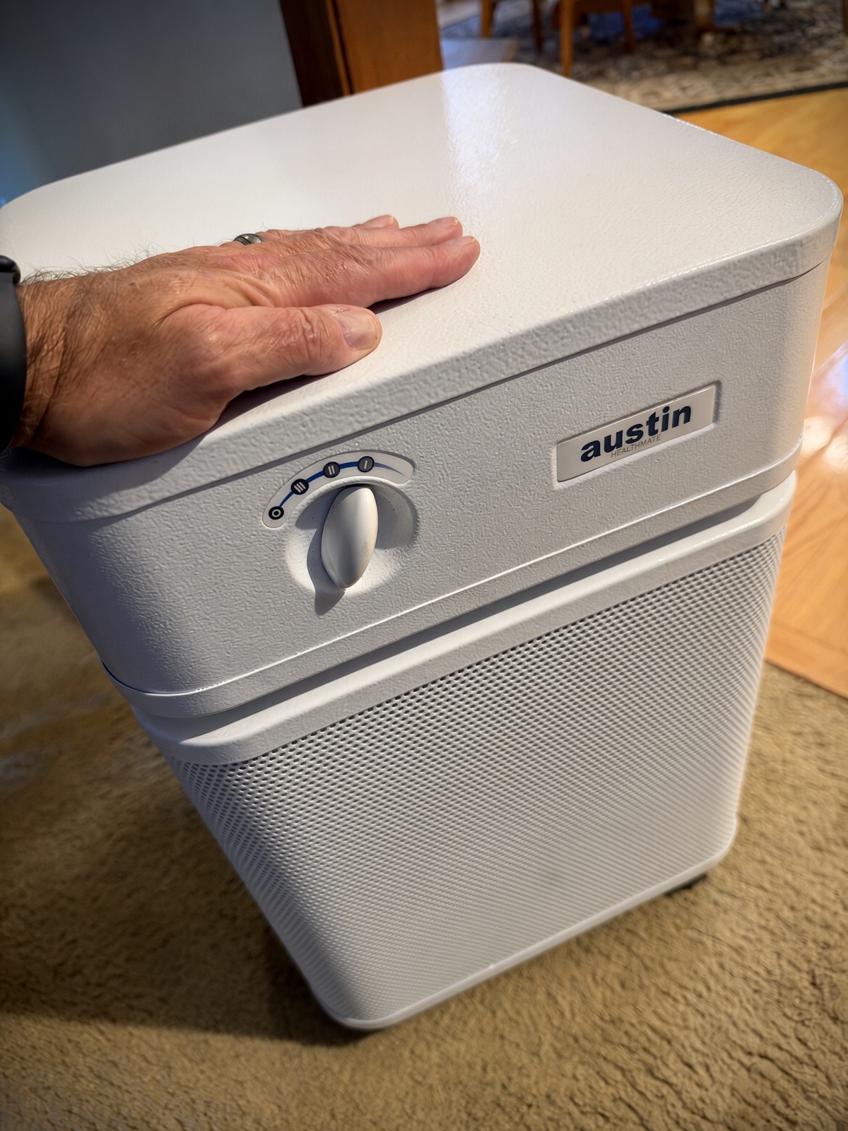Adult hand resting flat on top of a white Austin Air HealthMate air purifier to show its size