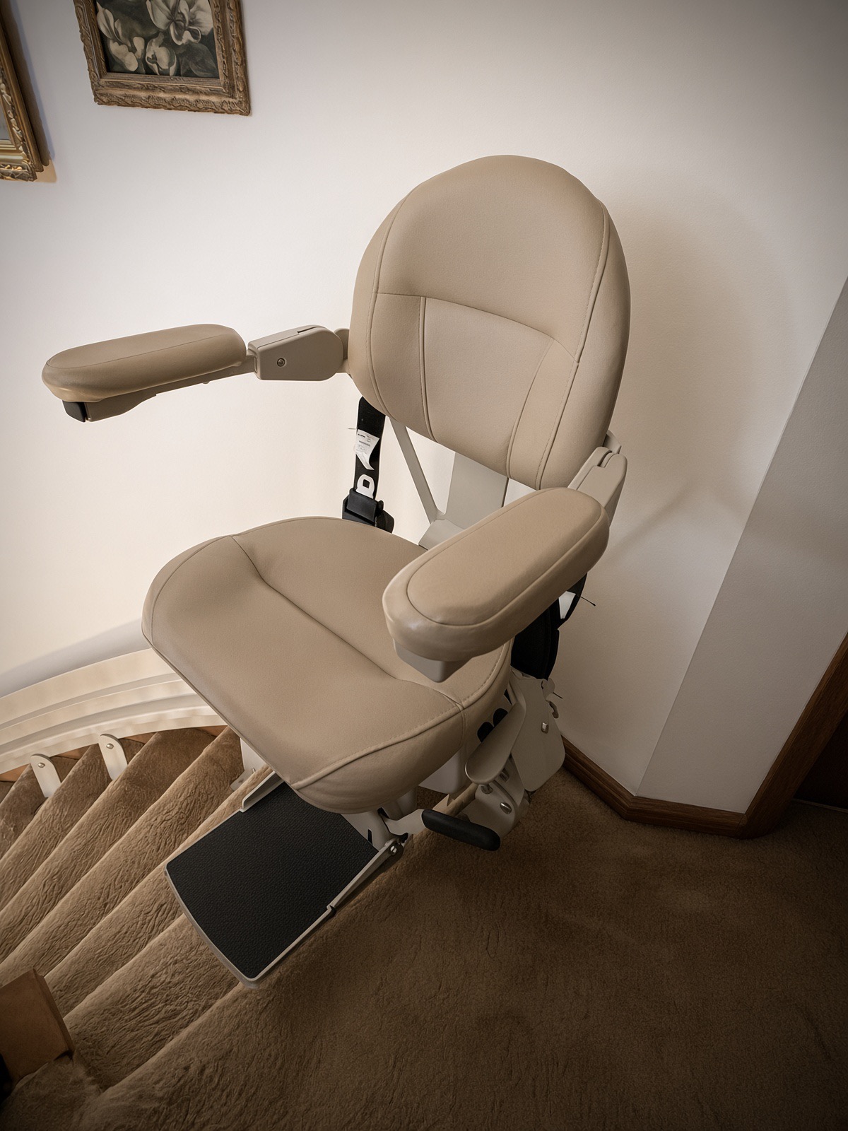 Beige stair chairlift seen from above at the top of a carpeted staircase