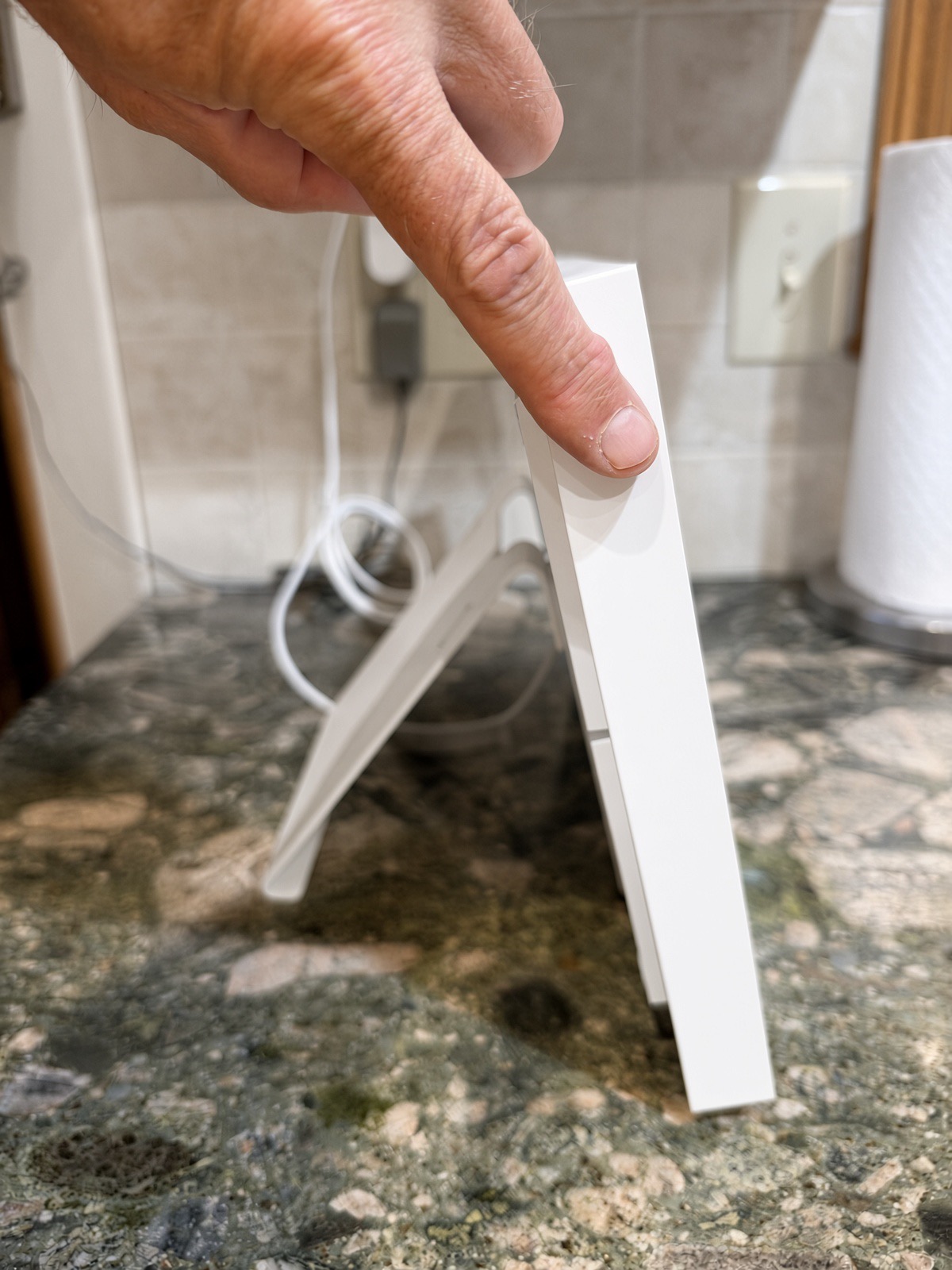 Side view of the Skylight Calendar standing on a granite counter on its fold-out kickstand, power cord plugged in behind it