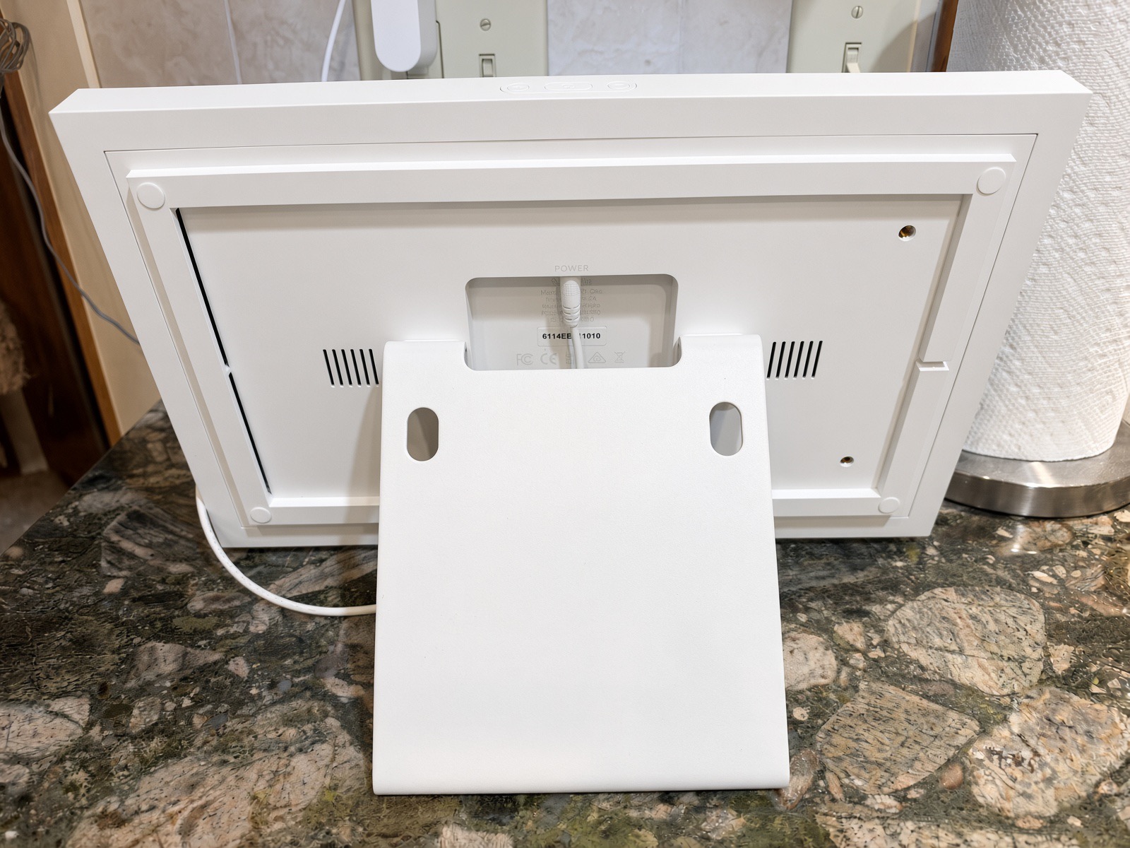 Back of the white Skylight Calendar showing the fold-out stand, vents and the power cord plugged into the center port