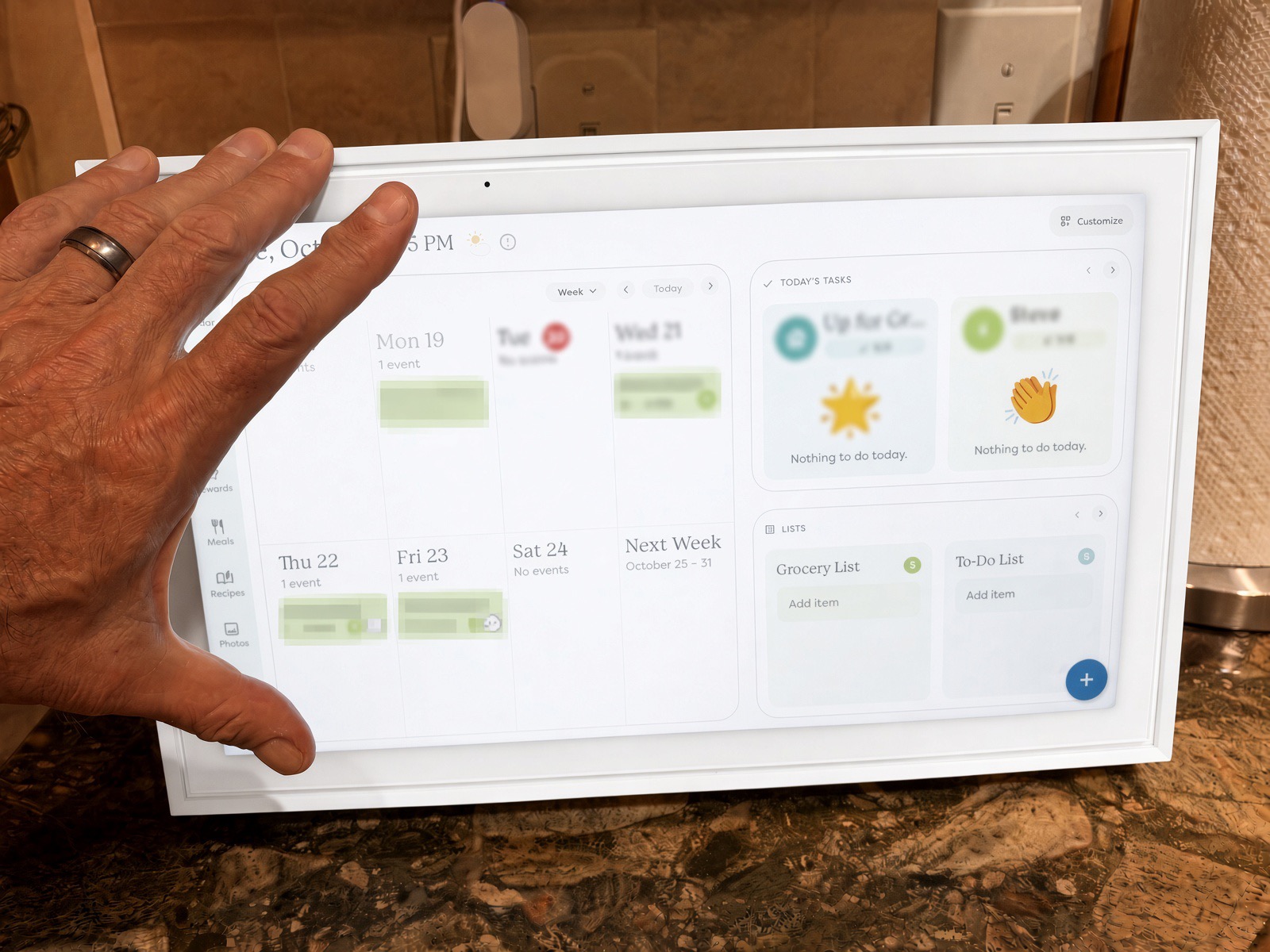 Hand reaching toward the Skylight Calendar home screen showing a week calendar, today’s tasks and grocery and to-do lists, details blurred
