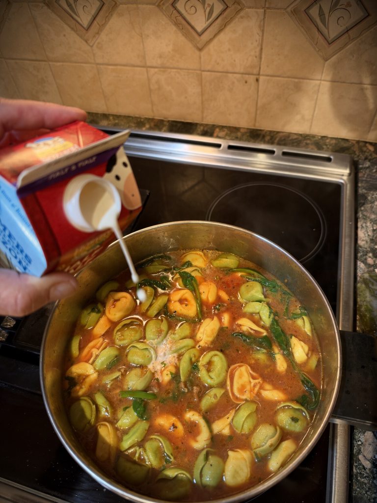 Heavy cream being poured into a pot of finished tortellini soup