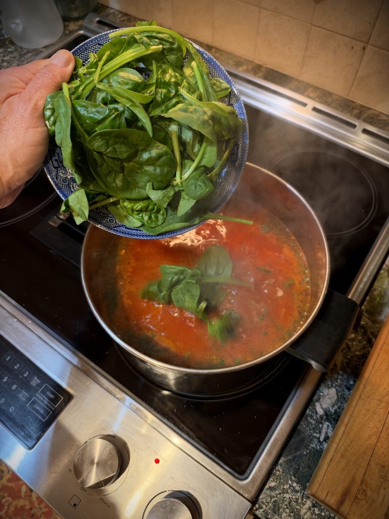 Fresh baby spinach being stirred into the hot soup to wilt