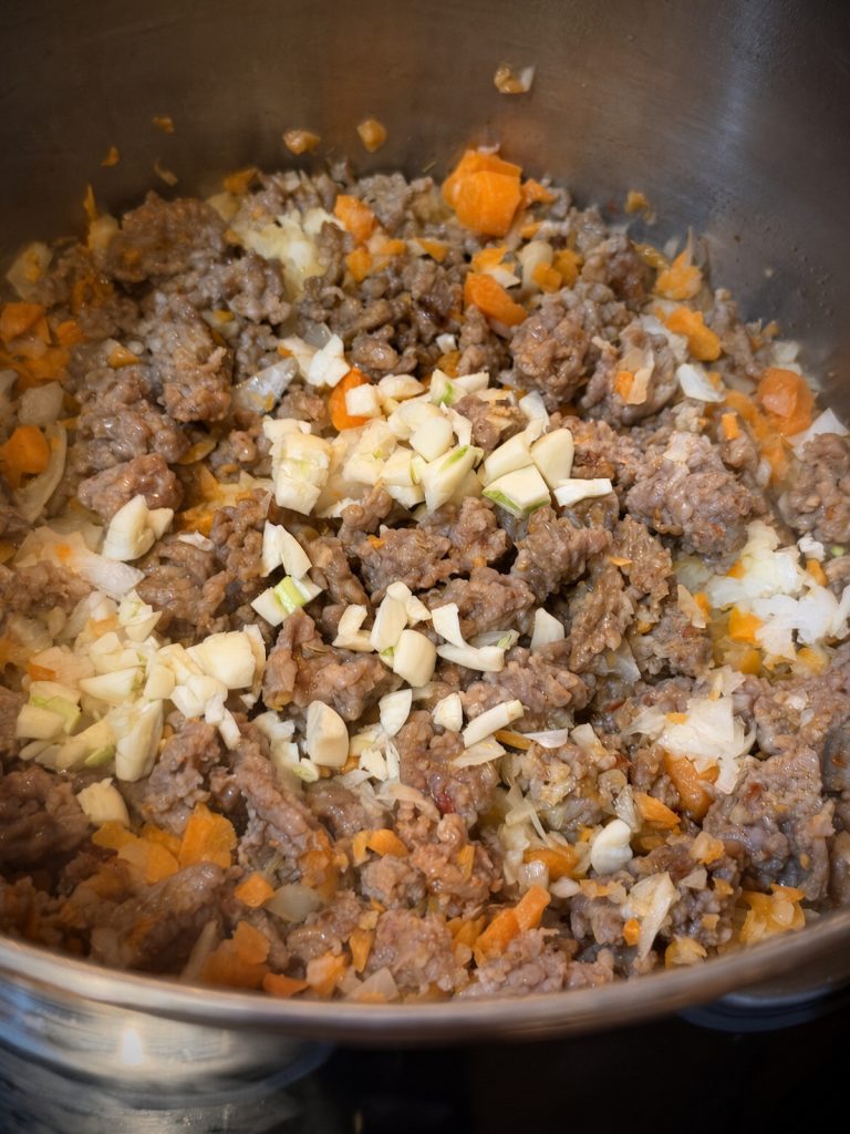 Close-up of browned sausage with softened onion, carrots, and garlic