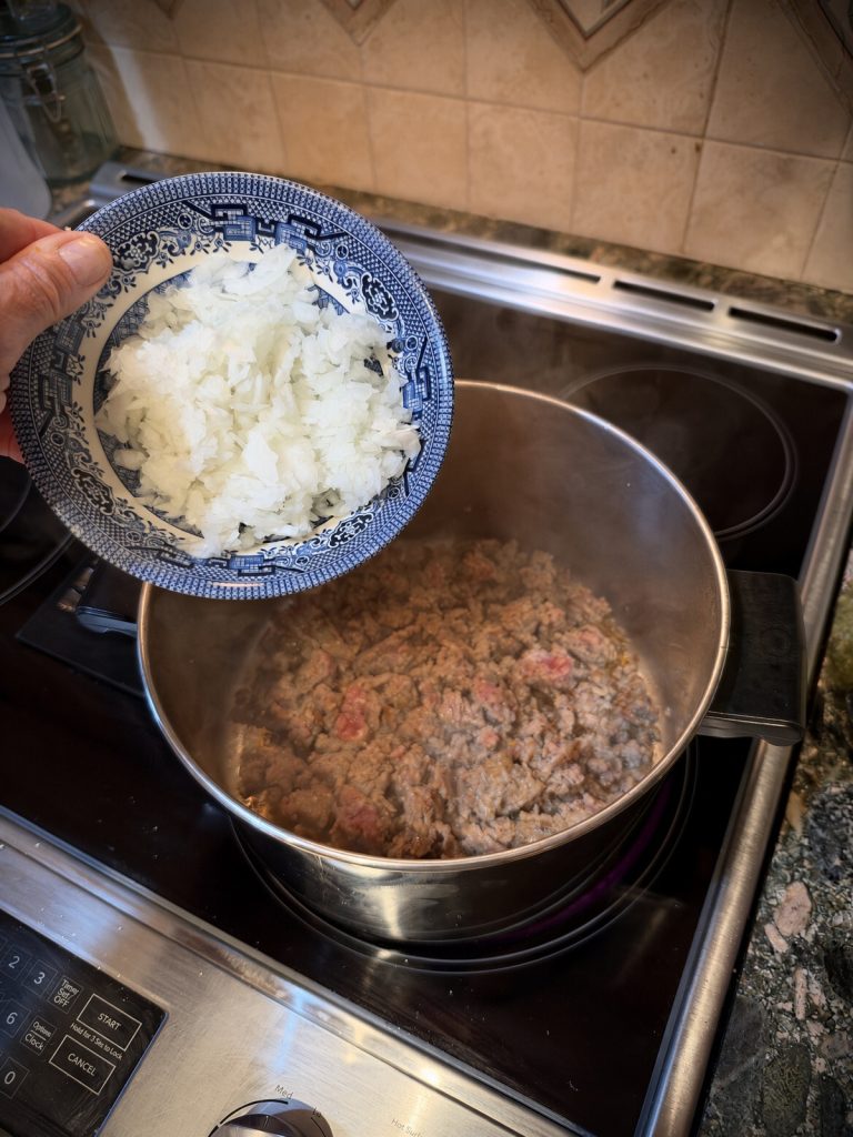 Diced onion added to the browned sausage in the pot