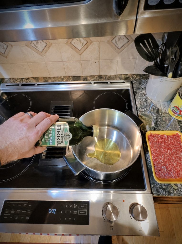 Olive oil being poured into a Dutch oven to brown the sausage