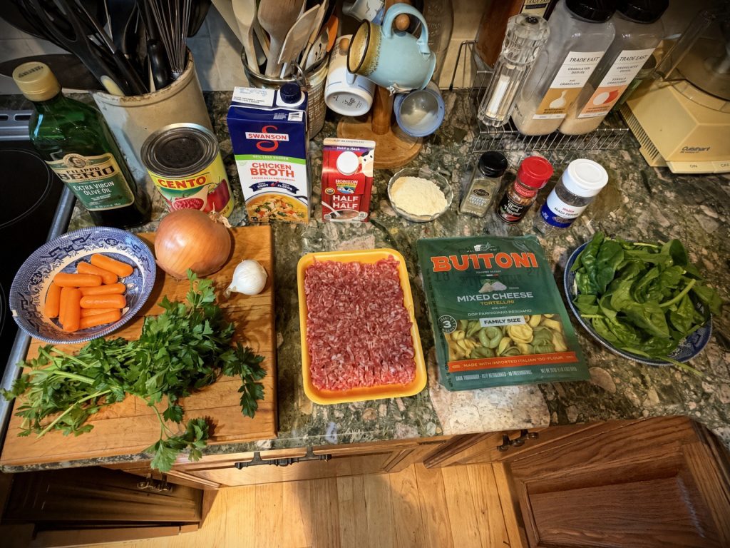Tortellini soup ingredients laid out on the counter: sausage, tortellini, crushed tomatoes, broth, spinach, and vegetables