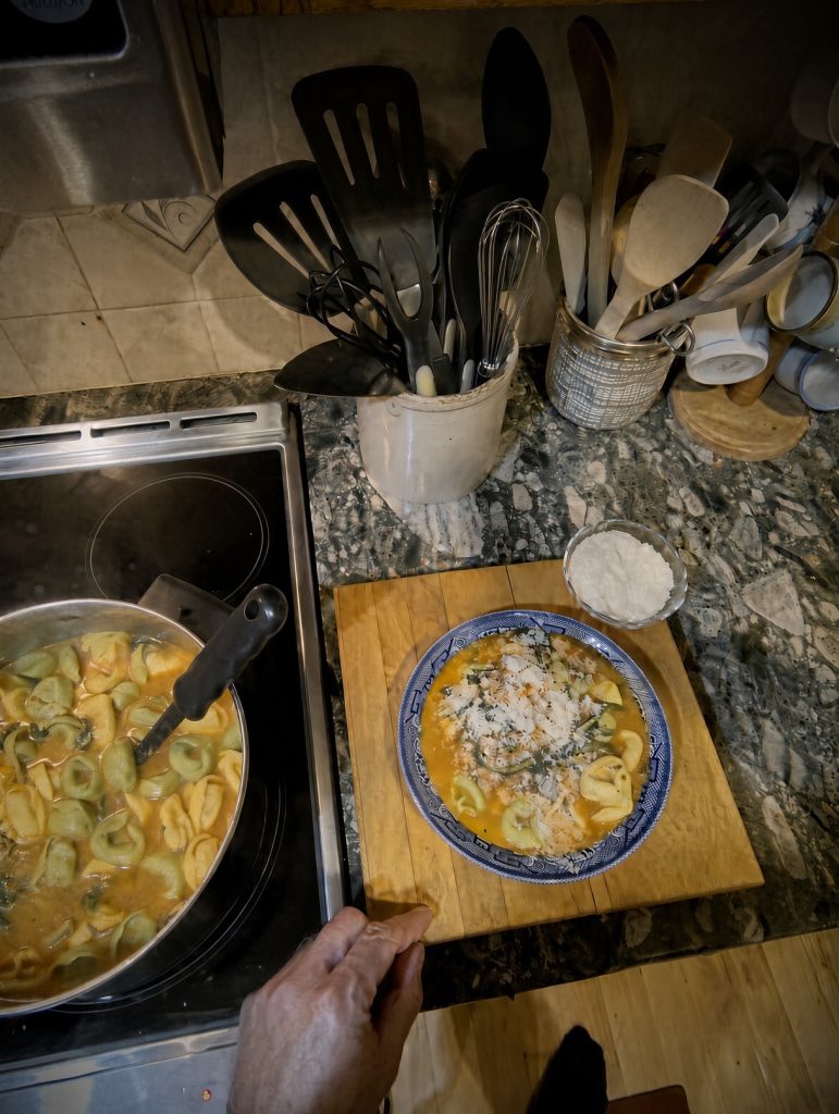 A bowl of tortellini soup topped with Parmesan next to the pot