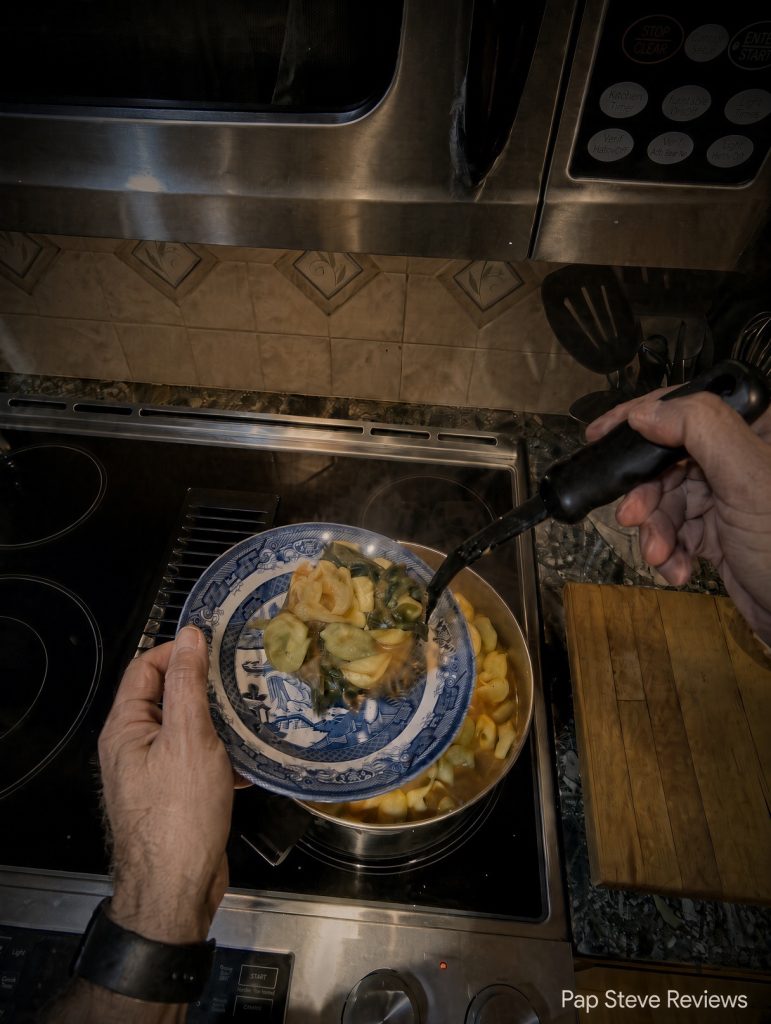 Ladling tortellini soup into a blue willow bowl