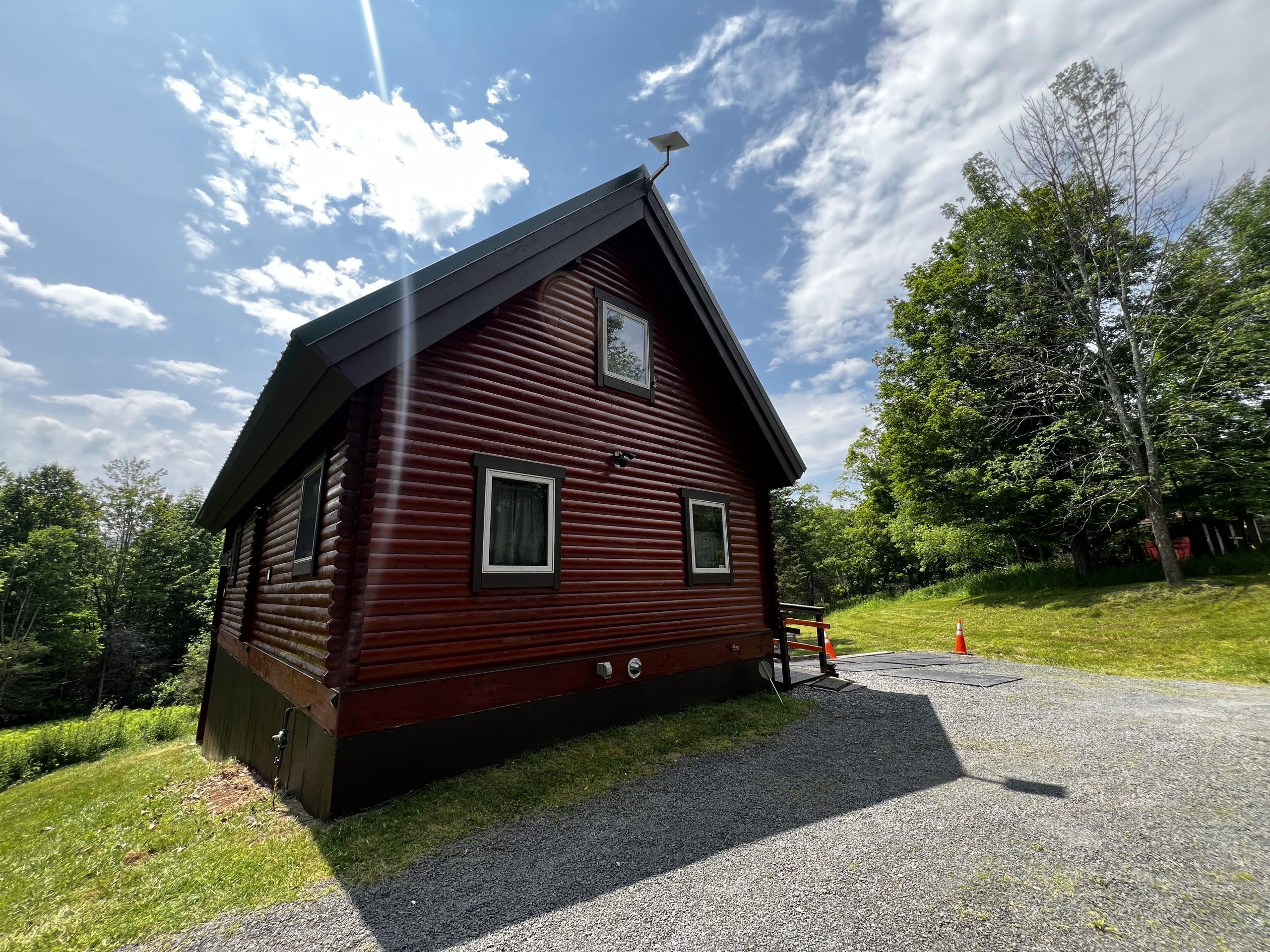 Front of Pap Steve's red log cabin with a green metal roof and gravel drive in the Catskills