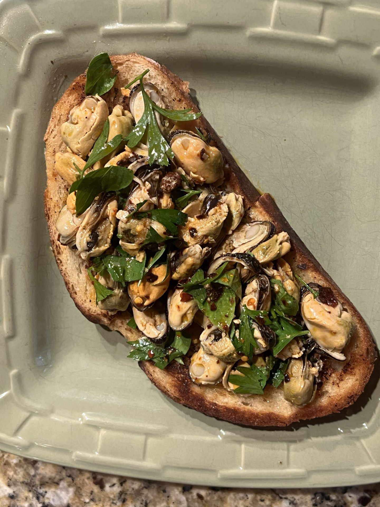 Mussel toast with lemon, chili oil, garlic and parsley on homemade Italian bread
