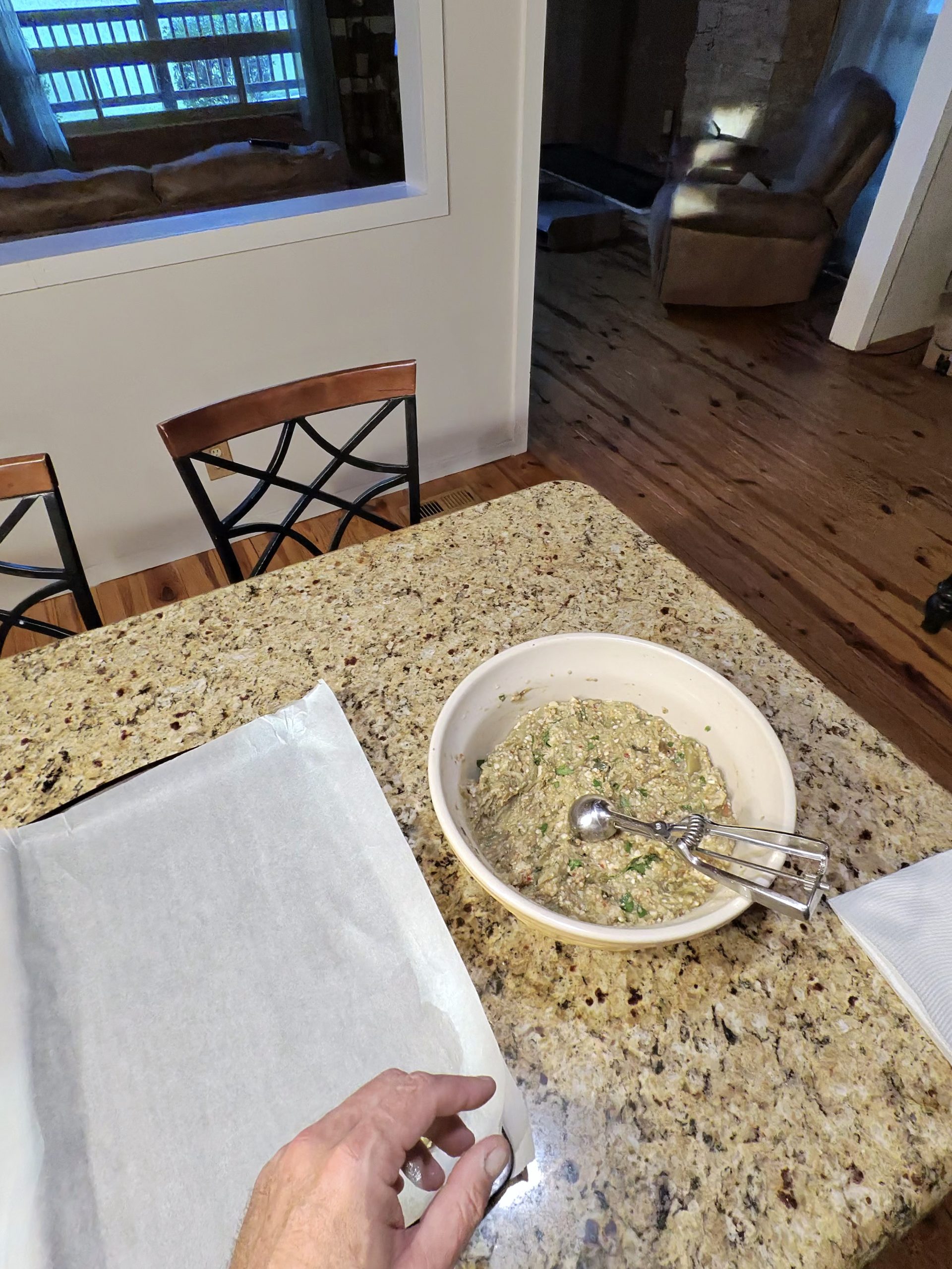 Bowl of Italian eggplant ball mixture with a cookie scoop, parchment being laid on a sheet pan