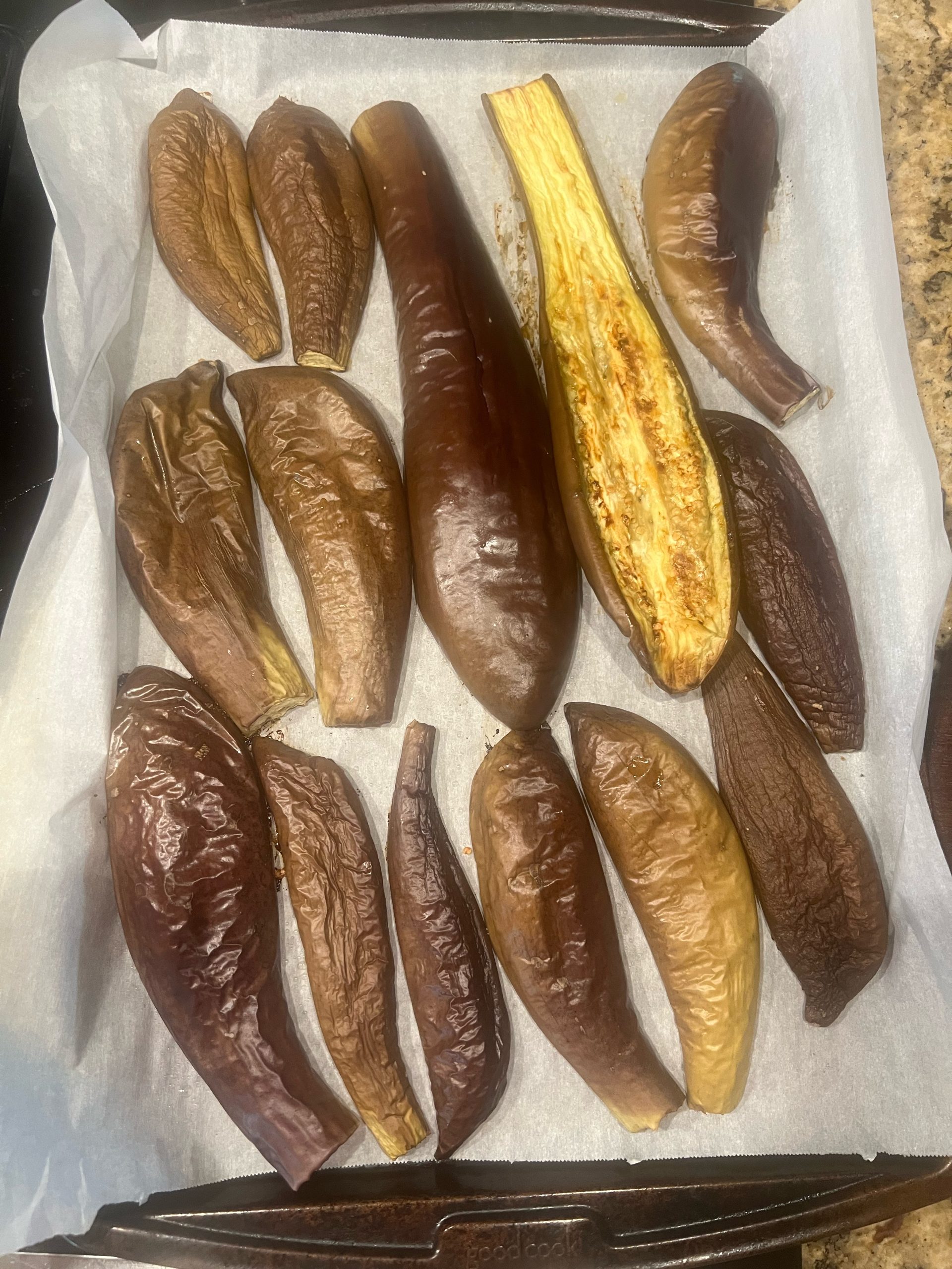 Homegrown eggplant halves roasted at 350 degrees on a parchment-lined sheet pan